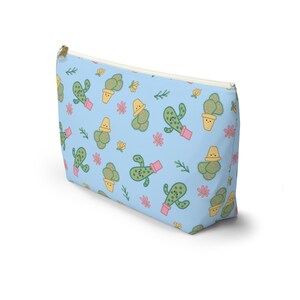 May include: A light blue zippered pouch with a repeating pattern of smiling cacti in yellow pots on a light blue background. The cacti are green with yellow flowers and pink accents.