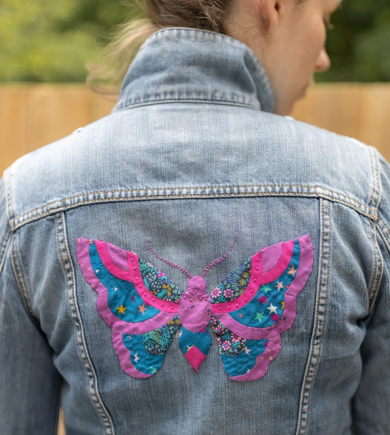 May include: A denim jacket with a colorful butterfly patch sewn on the back. The butterfly is made of fabric scraps in shades of pink, blue, and green.