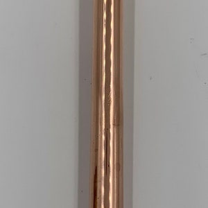 Puede incluir: Una herramienta de metal de color cobre con un gancho en el lateral y una punta puntiaguda. La herramienta tiene una superficie lisa y brillante.