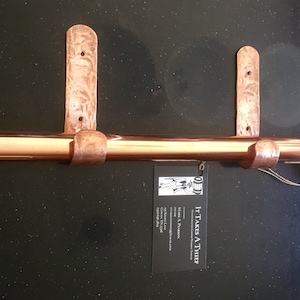 May include: A copper curtain rod with two hammered copper brackets. The rod is approximately 36 inches long and has a pointed end. The brackets are attached to the wall with screws. The rod is labeled "It Takes A Thinner".