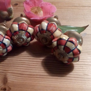 May include: Four ceramic cabinet knobs with a floral design. The knobs are white with red and blue accents. The knobs have a gold-colored metal base.