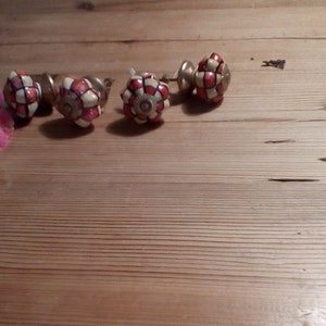 May include: Five ceramic drawer knobs with a white and red checkered pattern. The knobs have a gold metal base.