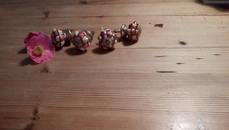 May include: Five ceramic drawer knobs with a white and red checkered pattern. The knobs have a gold metal base.