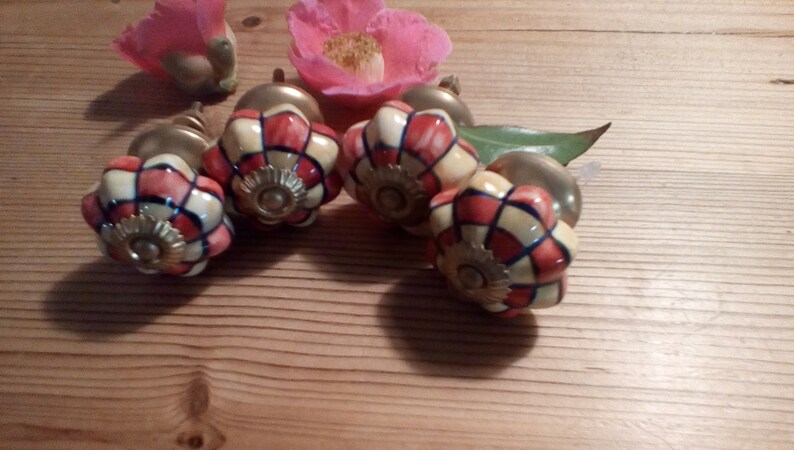May include: Four ceramic cabinet knobs with a floral design. The knobs are white with red and blue accents. The knobs have a gold-colored metal base.