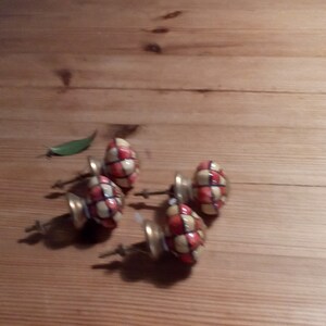 May include: Five ceramic cabinet knobs with a checkered pattern in red, white, and black. The knobs have a gold-colored metal base and screws.