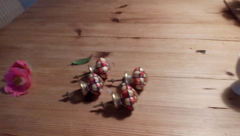 May include: Five ceramic cabinet knobs with a checkered pattern in red, white, and black. The knobs have a gold-colored metal base and screws.