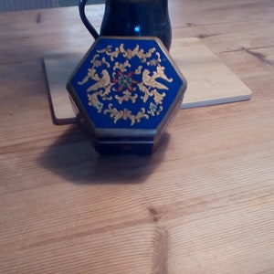 May include: A hexagonal blue music box with gold accents and a floral design. The box has a lid with a floral design and two birds.