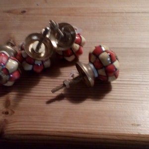 May include: Four ceramic cabinet knobs with a red and yellow checkered pattern. The knobs have a gold metal base and screw.