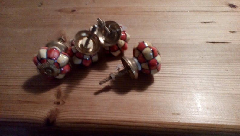 May include: Four ceramic cabinet knobs with a red and yellow checkered pattern. The knobs have a gold metal base and screw.