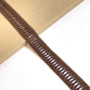 May include: Brown braided trim with a criss-cross pattern. The trim is made of a soft, flexible material and has a subtle sheen.