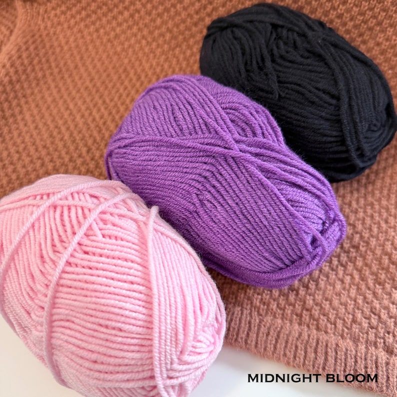 May include: Three skeins of yarn in pink, purple, and black are arranged on a textured, brown surface. The pink yarn is in the foreground, followed by the purple and black skeins. The text "MIDNIGHT BLOOM" is visible in the lower right corner.