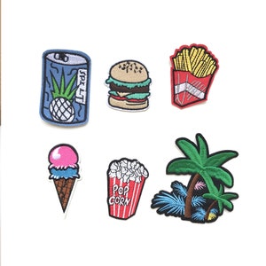 May include: A collection of embroidered patches featuring food and tropical themes. Includes a blue soda can with a pineapple, a hamburger, a container of fries, an ice cream cone, a popcorn container, and a palm tree.