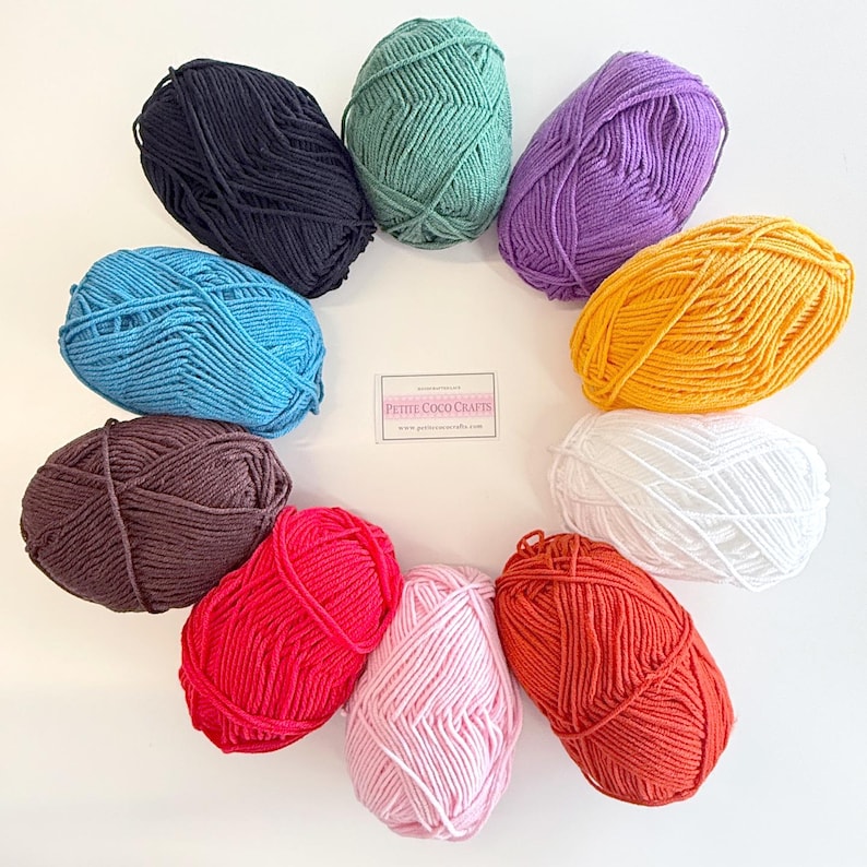 May include: A collection of colorful yarn skeins arranged in a circle. The yarn colors include black, teal, purple, yellow, white, orange, pink, red, brown, and blue. The image includes a small sign with the text "Petite Coco Crafts".
