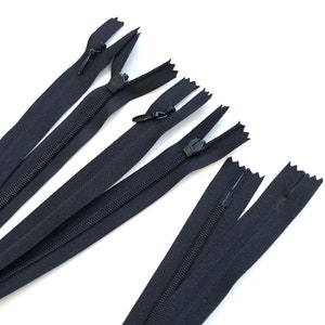 May include: Several black zippers are arranged diagonally against a white background. The zippers are closed, with the zipper pulls visible. The fabric of the zippers appears to be a sturdy, woven material. The image is well-lit, highlighting the details of the zippers.