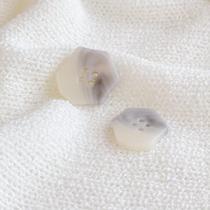 Może przedstawiać: Dwa białe i szare guziki z czterema otworami każdy. Guziki leżą na białym dzianym materiale.