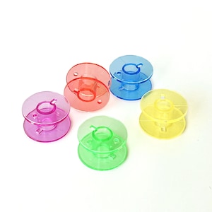 以下が含まれることがあります： ミシン用のカラフルなプラスチックボビン5個。ボビンはピンク、赤、青、黄、緑の色合いです。