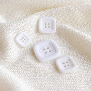 May include: Four white plastic buttons of different sizes. The buttons are square shaped with four holes each.