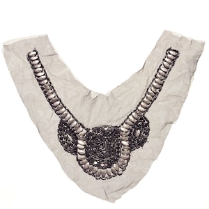 Könnte beinhalten: Eine silberne und schwarze Perlenverzierung für Kleidung. Die Verzierung ist V-förmig und hat ein zartes, filigranes Design.