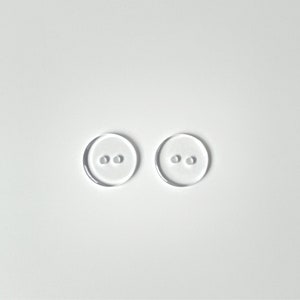 Puede incluir: Dos botones de plástico transparente con dos agujeros cada uno.