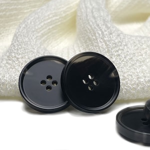 Puede incluir: Tres botones de plástico negro, cada uno con cuatro agujeros. Los botones son redondos y tienen un acabado brillante.
