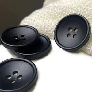 May include: Four black plastic buttons with four holes each. The buttons are round and have a slightly raised edge.