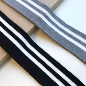 May include: Two pieces of black and gray knit fabric with white stripes. The fabric is ribbed and has a stretchy texture.