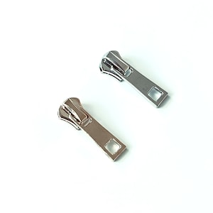 May include: Two metal zipper pulls, one silver and one gold, with a square opening at the bottom.