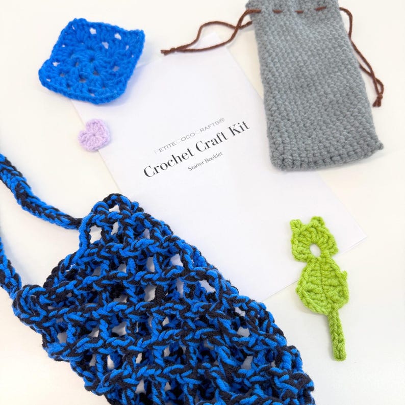 May include: A crochet craft kit with a blue and black net bag, a blue square, a gray drawstring pouch, a green leaf-shaped applique, a purple heart, and a booklet that reads "Crochet Craft Kit Starter Booklet."