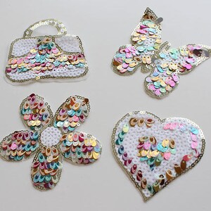 May include: Four colorful iron-on patches with a butterfly, a handbag, a flower, and a heart design. The patches are made of sequins and are perfect for adding a touch of sparkle to clothing, bags, or other accessories.