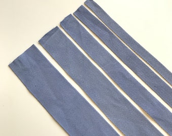 May include: Five different lengths of light blue twill tape, arranged in a diagonal line on a white surface.