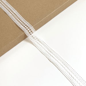 May include: White lace trim with a delicate pattern. The trim has a scalloped edge and is perfect for adding a touch of elegance to any project.