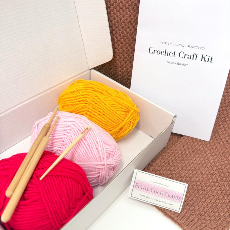 May include: A crochet craft kit in an open white box, containing three balls of yarn in red, pink, and yellow, along with wooden crochet hooks. A white booklet with the text "Crochet Craft Kit" is visible, along with a small business card.