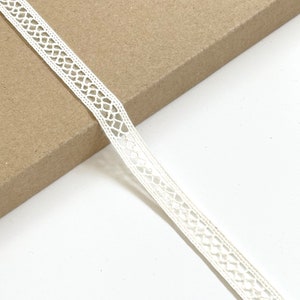 Puede incluir: Borde de encaje blanco con un patrón delicado. Esta cinta es perfecta para agregar un toque de elegancia a cualquier proyecto.