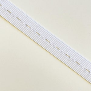 以下が含まれることがあります： 縫製用のボタンホールが均等に間隔をあけて配置された白いゴム。このゴムは、調節可能な衣服を作るのに最適です。