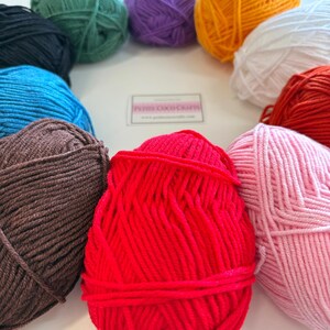May include: A collection of colorful yarn balls in various shades, including red, pink, brown, blue, green, purple, orange, and white. The yarn is arranged in a circular pattern, with a small sign in the center that reads "Petite Coco Crafts".