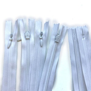 May include: Several white nylon zippers with matching pulls are arranged against a white background. The zippers are closed and open, showcasing the teeth and the slider mechanism. These zippers are suitable for various sewing projects.