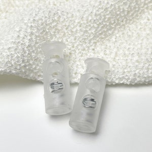 Puede incluir: Dos topes de palanca de plástico transparente con un resorte metálico en el interior. Los topes están diseñados para usarse con cordones o correas.