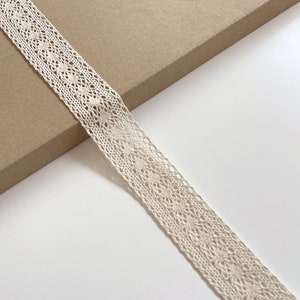 May include: A close-up of a cream-colored crocheted lace trim. The lace has a delicate, intricate pattern.