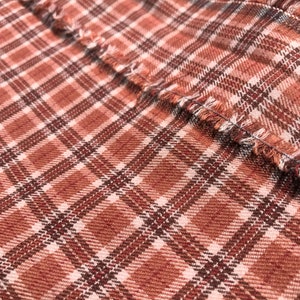 May include: Close-up of a brown and white plaid fabric with a frayed edge.