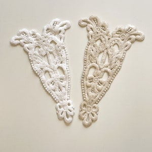 Puede incluir: Dos aplicaciones de encaje blanco con un delicado diseño floral. La aplicación de la izquierda es blanca y la aplicación de la derecha es de color crema.