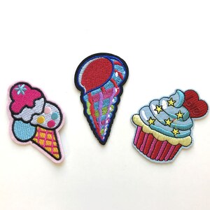 May include: Three embroidered iron-on patches featuring a blue and white cupcake with a red heart, a pink and blue ice cream cone, and a colourful ice cream cone.