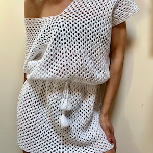 Può includere: Abito bianco all'uncinetto con scollatura monospalla e maniche corte. L'abito presenta una vita con coulisse e dettagli a nappe. Il design a trama aperta crea un look leggero e arioso. Perfetto per la spiaggia o le vacanze.