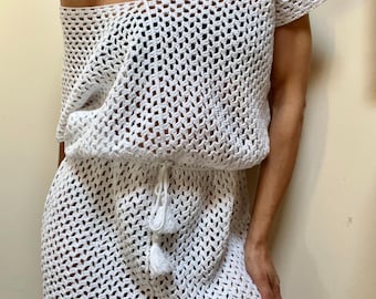 May include: White crochet dress with an off-the-shoulder neckline and short sleeves. The dress features a drawstring waist with tassel details. The open weave design creates a light and airy look. This handmade dress is perfect for beach or resort wear.