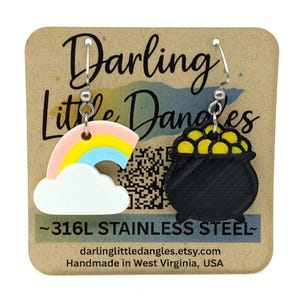 May include: A pair of dangle earrings featuring a rainbow and a pot of gold. The rainbow is in pastel colors, and the pot of gold is black with yellow coins. The earrings are made of 316L stainless steel.