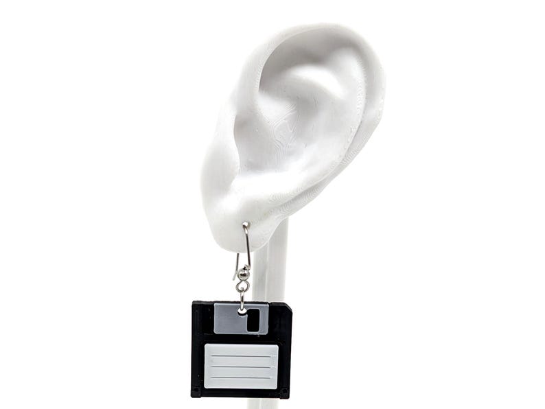 May include: A pair of novelty earrings featuring a black and gray floppy disk design. The earrings hang from silver-colored hooks, offering a unique and retro aesthetic. The earrings are a fun accessory for those who appreciate vintage tech.