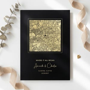 Puede incluir: Impresión enmarcada en negro con un mapa dorado de una ciudad, marcado con un corazón. Debajo, el texto dice "WHERE IT ALL BEGAN", seguido de nombres y una fecha. Un elemento decorativo.