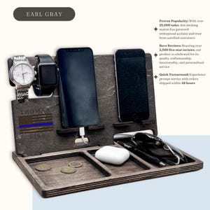 May include: A wooden docking station with slots for two phones, a watch, and a pair of glasses. It also has a small tray for keys or other small items. The station is personalised with the name "THOMAS" and the number "9198".