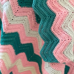 Könnte beinhalten: Eine gehäkelte Decke mit einem Chevron-Muster in Rosa, Weiß und Türkis.