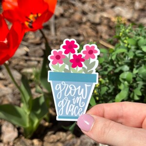 May include: A sticker with a blue flower pot and pink flowers. The text "grow in grace" is written in white on the pot.