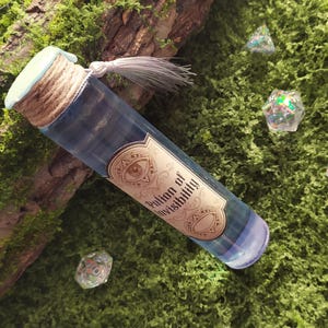 Pode incluir: Uma garrafa de poção de vidro com líquido azul e um rótulo que diz "Potion of Invisibility". A garrafa é selada com uma rolha verde clara, barbante e uma borla. Dados iridescentes transparentes sobre musgo verde.